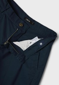 Pantalones azul marino con una textura suave, que cuentan con una cremallera en la bragueta, cierre de botón y una etiqueta marcada como 'LMTD.' Se visible un bolsillo interior.