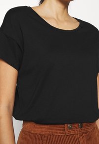 Černé tričko s krátkým rukávem a kulatým výstřihem, vyrobené z měkké látky, s volným střihem a jemnými bočními rozparky, spárované s manšestrovými kalhotami.