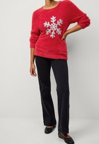 Pull rouge en peluche avec un grand motif de flocon de neige argenté sur le devant. Assorti à un jean noir évasé et des ballerines noires.