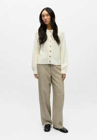 Valge kootud kardigan tekstuurse mustriga, ümar kaelus ja hõbedased nööbid. Sobitatud beežide laia säärega pükstega ja mustade mokassiinidega.