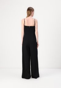Combinaison noire avec des fines bretelles, une fermeture éclair au dos et des jambes larges et fluides en tissu léger.