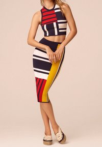 Dvoudílný outfit složený z crop topu a tužkové sukně. Materiál má výrazné vzory v námořnické modré, červené, žluté a bílé barvě. Textura je hladká a dobře padnoucí.