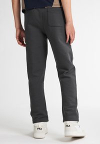 Mörkgrå sweatpants med en slät yta, rak skärning och elastisk midja. Ett par vita sneakers med synlig logotypdetalj.