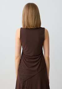 Abito senza maniche di colore marrone realizzato in tessuto morbido, caratterizzato da un design drappeggiato con dettagli in pizzo sulla gonna e una texture liscia.