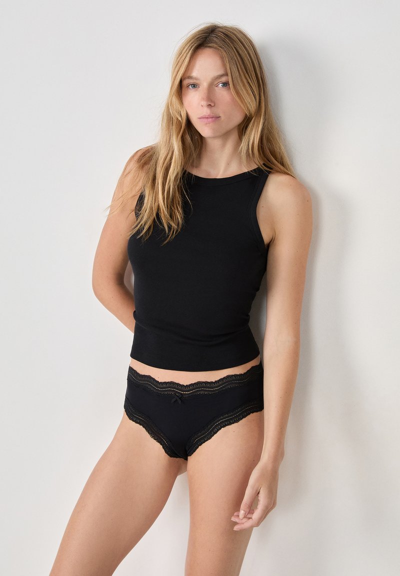 Top in cotone nero a maniche corte e mutandine neri con pizzo e dettaglio a fiocco, con una texture liscia e una vestibilità aderente. Presenta un approccio di design minimalista.