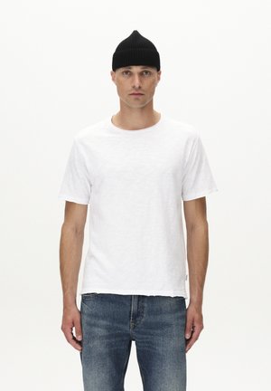 Biały t-shirt z okrągłym dekoltem, wykonany z teksturowanej tkaniny, w połączeniu z niebieskimi dżinsami. Model nosi czapkę beanie z prążkowanego materiału w kolorze czarnym. Proste tło.