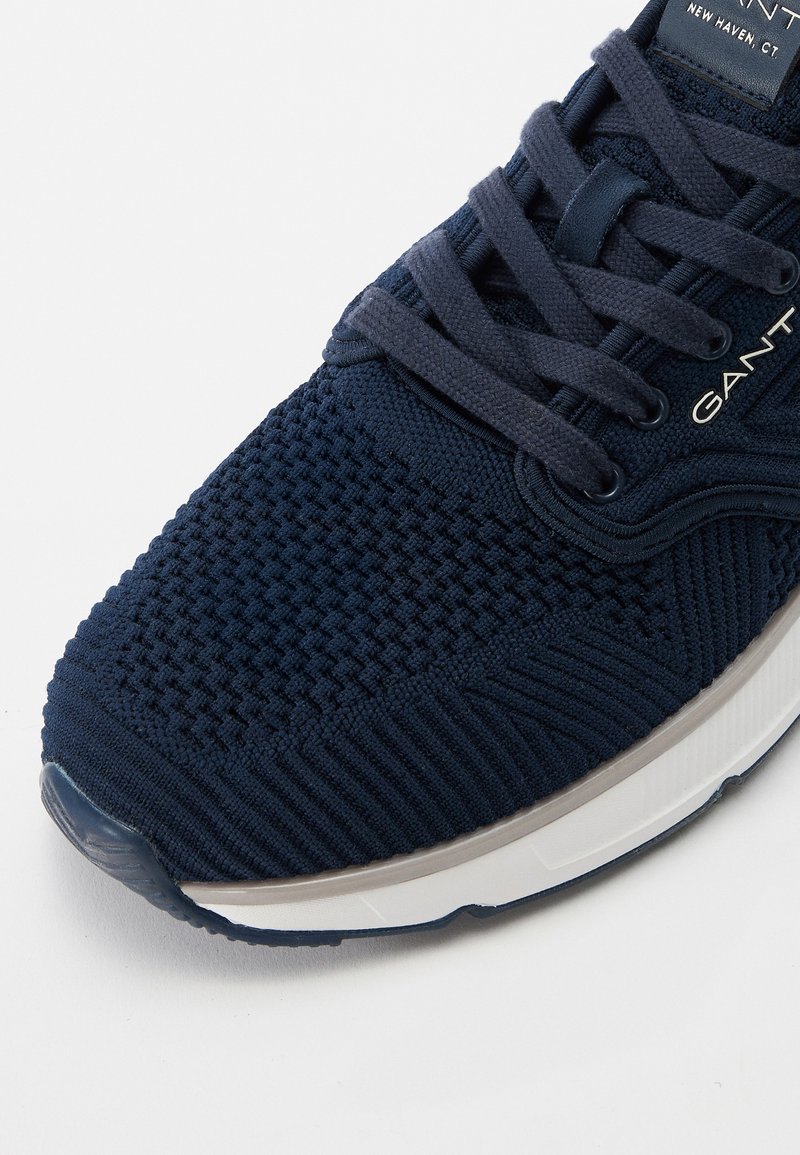 Marineblaue gestrickte Sportschuhe mit strukturiertem Obermaterial, passenden Schnürsenkeln, gepolsterter Sohle und dezentem Logodetail an der Seite.