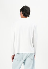 Witte langekorte mouwen shirt van zachte katoen, met een ronde halslijn en rechte zoom, gecombineerd met lichtblauwe jeans.