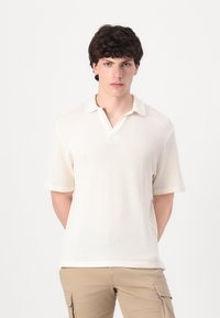 Vaffel-strukturert polo-skjorte med korte ermer i kremfarge, med krage og delvis åpen flenge, kombinert med beige cargo bukser.