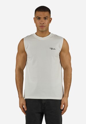 Νεαρός άνδρας που φοράει λευκό αμάνικο πουκάμισο με μικρό μαύρο καλλιγραφικό λογότυπο "Pegador" στο στήθος, στέκεται μπροστά σε απλό λευκό φόντο.