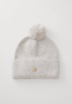 Bonnet tricoté gris clair avec un grand pom-pom en fausse fourrure sur le dessus et un petit logo doré en accent à l'avant. Design à côtes texturées.