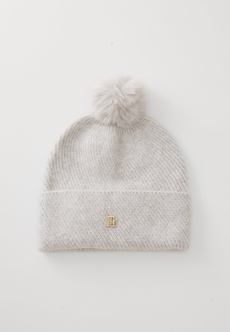 Lichtgrijze gebreide beanie met een grote nepmof bovenop en een klein gouden logoaccent aan de voorkant. Getextureerd geribbeld ontwerp.