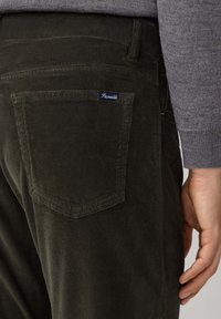 Donkergroene corduroy broek met een gestructureerd oppervlak, voorzien van een achterzak en een klein blauw label dat aan de naad van de zak is geplaatst.