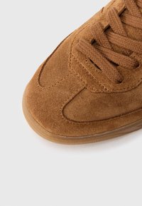 Καφέ δερμάτινο αθλητικό παπούτσι με στρογγυλεμένη μύτη, υφασμάτινο επάνω μέρος με υφή και επίπεδα καφέ κορδόνια. Λαστιχένια σόλα με λείο φινίρισμα.