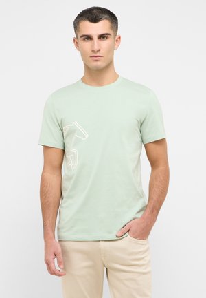 Light green cotton t-shirt featuring a white silhouette of a horse on the left side, round neckline, and short sleeves, paired with beige pants.