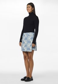 Svart ribbestrikket turtleneck genser paret med en blå denim miniskjørt med hvit blomsterbroderi og frynser. Svart loafers fullfører antrekket.
