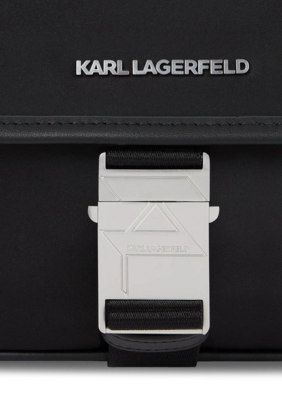 Близък план на черна чанта Karl Lagerfeld с голяма сребриста геометрична закопчалка и съответстващ надпис на марката.
