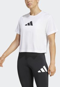 Bijela skraćena majica s crnim trokutastim logotipom, u kombinaciji s crnim tajicama koje imaju bijele dijagonalne pruge. Mekani, lagani materijal.