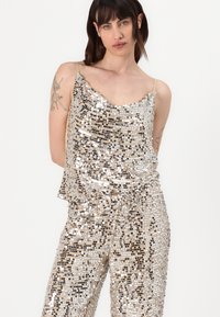 A sequined top and pants set featuring a scoop neckline, thin straps, and a mix of silver and gold sequins with a loose, draped fit.