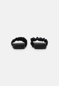 Black sandals with a textured rubber sole and scrunched fabric straps. Straps are soft, elastic, and loop around the foot comfortably.