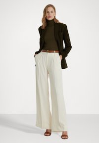 Donkergroene turtleneck, zwarte blazer, crème wijde broek met hoge taille, bruine riem en bruine sandalen met open tenen. Soepele texturen en een goede snit.