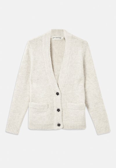 Κρεμ με πλεκτή ζακέτα με μακριά μανίκια, δύο μπροστινές τσέπες και τρία μαύρα κουμπιά σε σχήμα λουλουδιού κατά μήκος του κεντρικού μπροστινού μέρους.