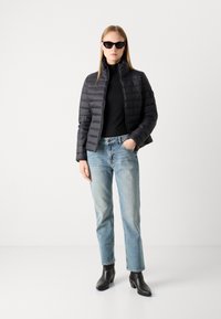 Doudoune noire avec un col montant, une coupe ajustée et des coutures horizontales, accompagnée d'un col roulé noir, d'un jean bleu clair et de bottes noires.