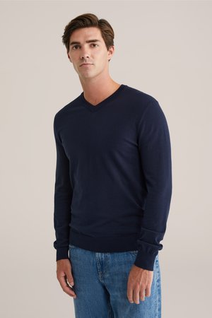 Svetarella a V-collo blu navy realizzata in tessuto morbido, con maniche lunghe e polsini a costine, abbinata a jeans azzurri.