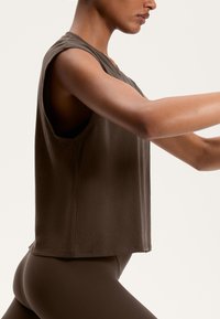 Barna ujjatlan, rövidített fazonú felső, kerek nyakkivágással, puha tapintással és laza illeszkedéssel. Az anyag könnyűnek tűnik, és kissé redőzött.