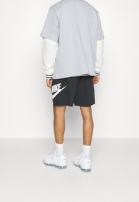 Grå överdimensionerad t-shirt med vita ärmar, svarta Nike-shorts med en vit logotyp, och vita sportskor med genomskinliga sula.