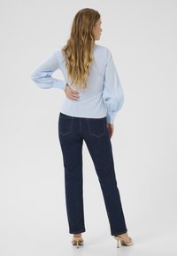 Ljust blå skjorta med puffärmar och långa ärmar, kombinerad med mörk denimjeans. Skjortan har en figursydd design och en mjuk textur.
