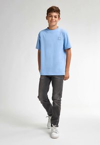 Tricou bleu deschis din bumbac, cu mâneci scurte, gât rotund și o mică aplicație cu logo. Asortat cu blugi gri închis și adidași albi.