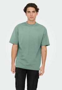 T-shirt en coton vert menthe avec manches courtes, col ras du cou et coupe décontractée, associé à un pantalon cargo noir avec poches latérales.