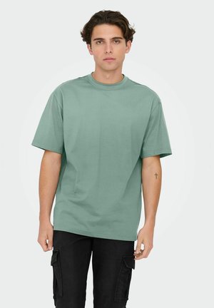 T-shirt en coton vert menthe avec manches courtes, col ras du cou et coupe décontractée, associé à un pantalon cargo noir avec poches latérales.