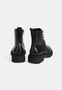 Zwarte leren enkelboots met een ronde neus, gestructureerd oppervlak, vetersluiting aan de voorkant en een ritssluiting aan de achterkant, voorzien van een stevige zool.