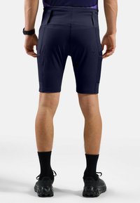 Shorts de sport navy avec une coupe ajustée, deux poches latérales et un tissu texturé. Portés avec des chaussettes et des chaussures noires. Vue arrière affichée.