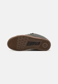 Scarpa in suede grigia con suola in gomma testurizzata, caratterizzata da un motivo geometrico e un marchio sul lato. I lacci sono passati attraverso i passanti.