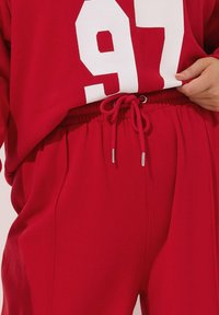 Rode sweatpants met een elastische tailleband en een trekkoord met zilveren uiteinden, gecombineerd met een bijpassend oversized shirt met een groot wit nummer 97.