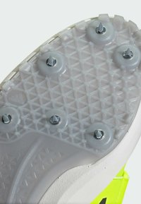 Suola di scarpa sportiva bianca con superficie in gomma testurizzata, perni esagonali e hardware argentato per la presa. Accenti di un vivace verde neon visibili.
