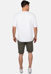Witte t-shirt met korte mouwen en ronde hals, gecombineerd met olijfgroene korte broek en witte sneakers, gezien van achter.