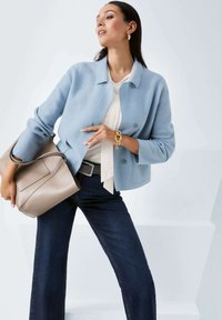 Light blue wool-blend jacket with a collar, round buttons, and three-quarter sleeves. Paired with dark jeans and a beige handbag.