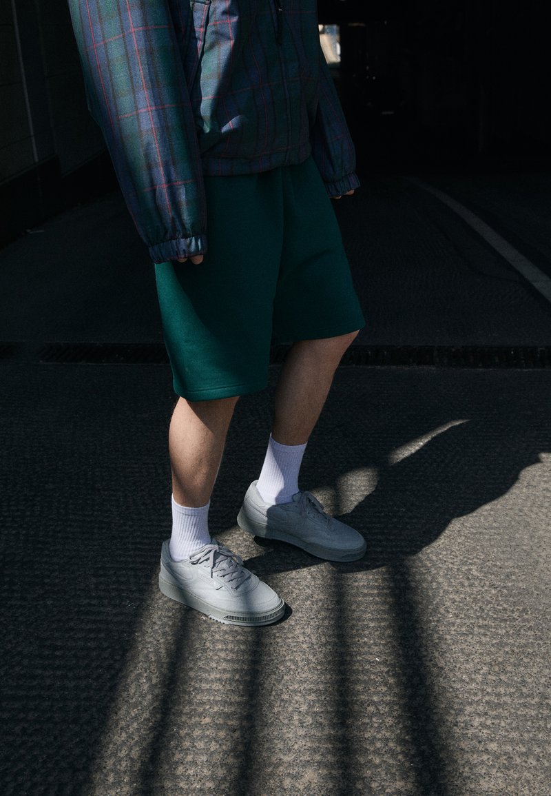 Grå sneakers, gröna shorts och vita strumpor. Oversized rutjacka i blå och vinröda nyanser. Skuggad yta med strukturerat mönster.