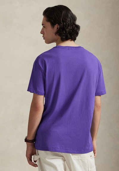 T-shirt en coton violet à manches courtes et encolure ronde, avec une coupe décontractée et des détails de couture minimalistes sur l'encolure et les ourlets.