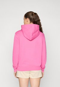 Rosa hettegenser med kengurulomme, ribbede ermer og kant. Myk bomullsblanding, glatt tekstur, og romslig hette.