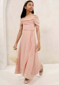 Roze, vloerlange jurk met off-the-shoulder pofmouwen, geplooid lijfje en bewerkte accenten. Gecombineerd met een parelendoos en sprankelende schoenen.