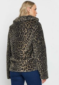 Leopardmönstrad fuskpälsjacka med hög krage, långa ärmar och sidfickor. Mjuk textur med svarta fläckar på en beige bakgrund.