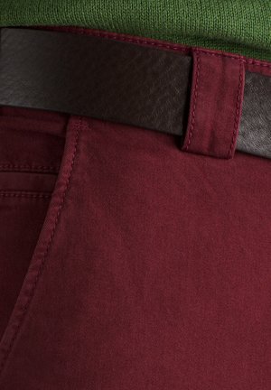 Pantalons bordeaux en tissu lisse, agrémentés d'une ceinture en cuir marron foncé et de coutures contrastées le long des poches.