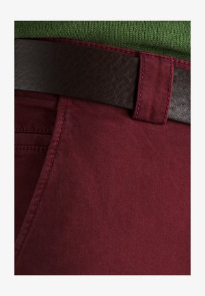 Burgunderfarbene Hose aus glattem Stoff, verziert mit einem dunkelbraunen Ledergürtel und kontrastierenden Nähten entlang der Taschen.