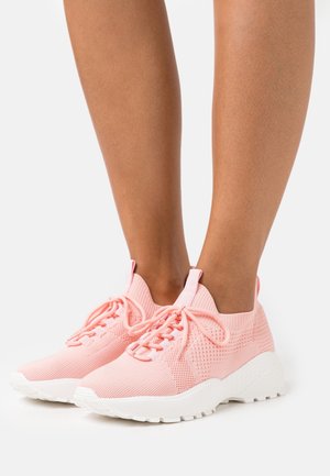 Baskets tricotées roses claires avec semelles blanches épaisses portées pieds nus, vues de face et de côté sur un fond blanc.