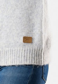 Maglione lavorato a maglia di un grigio chiaro con fondo a coste e un'etichetta in pelle che mostra "SWEDEMOUNT". Texture morbida con una leggera variazione di colore.